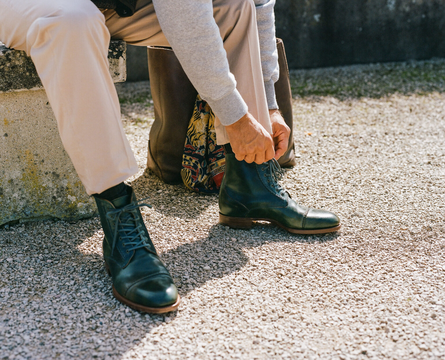 A gentleman sitting on patio steps tying up the laces of an E.Woodford Barrack 'Stanley' WWII Boot in Black Marbled Horween Shell Cordovan