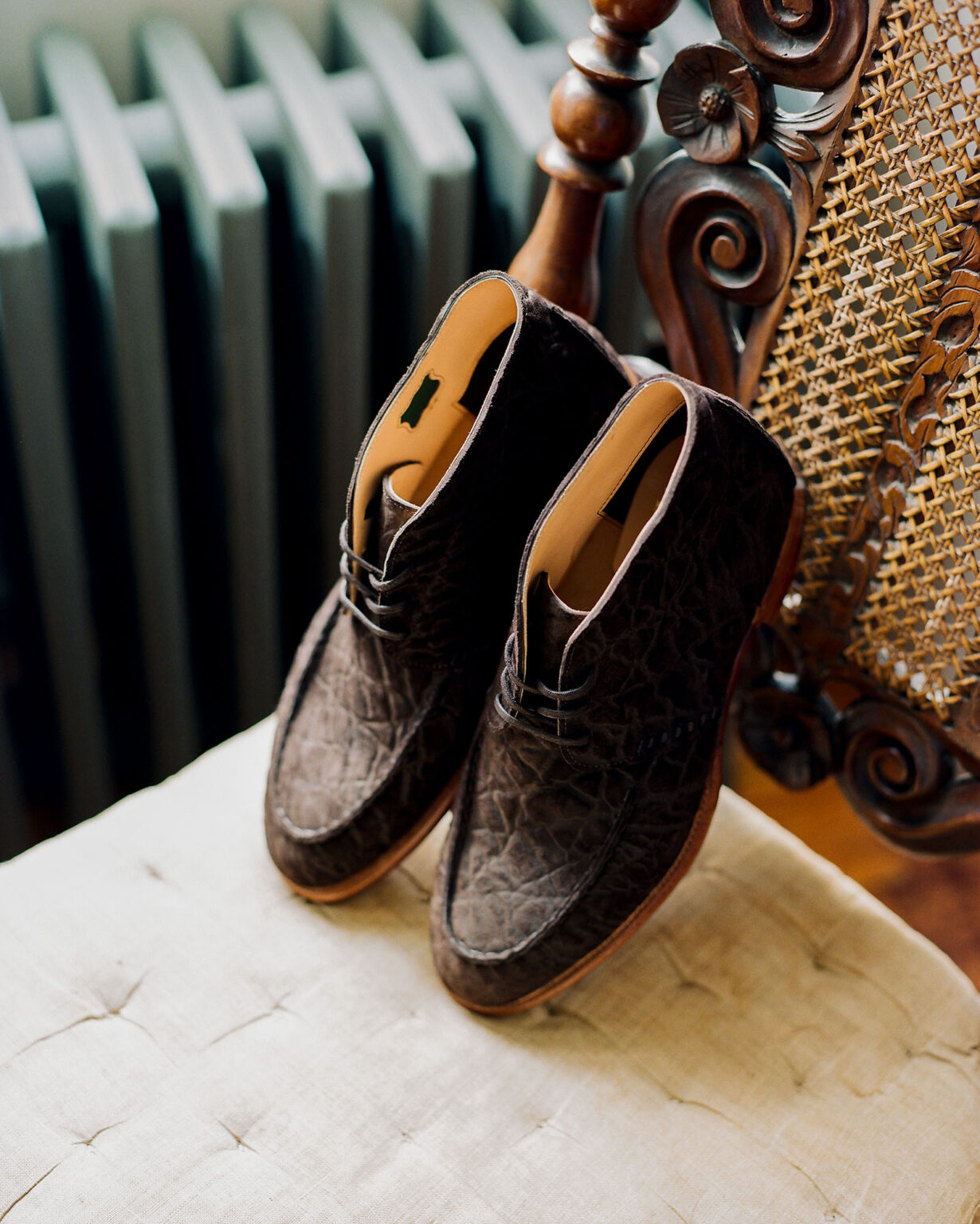 A pair of E.Woodford Edgware Ankle Boots in Bitter Chocolate CF Stead Janus Calf leather sitting on a vintage chair