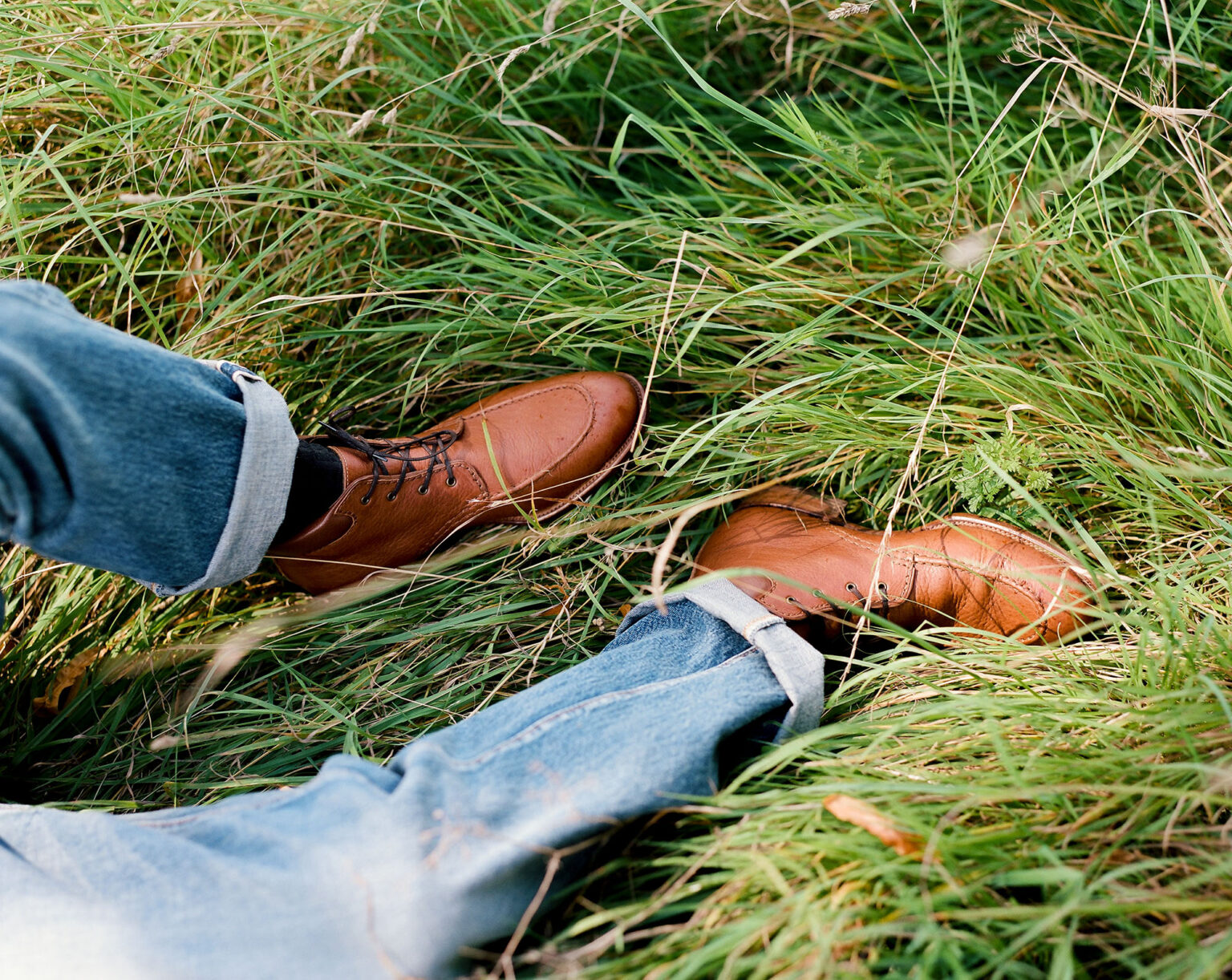 Gentleman laying down in long grass wearing turned up denim jeans and a pair of E.Woodford Foxley Padded Ankle Boots in Tan Horween Veg Tanned Bison