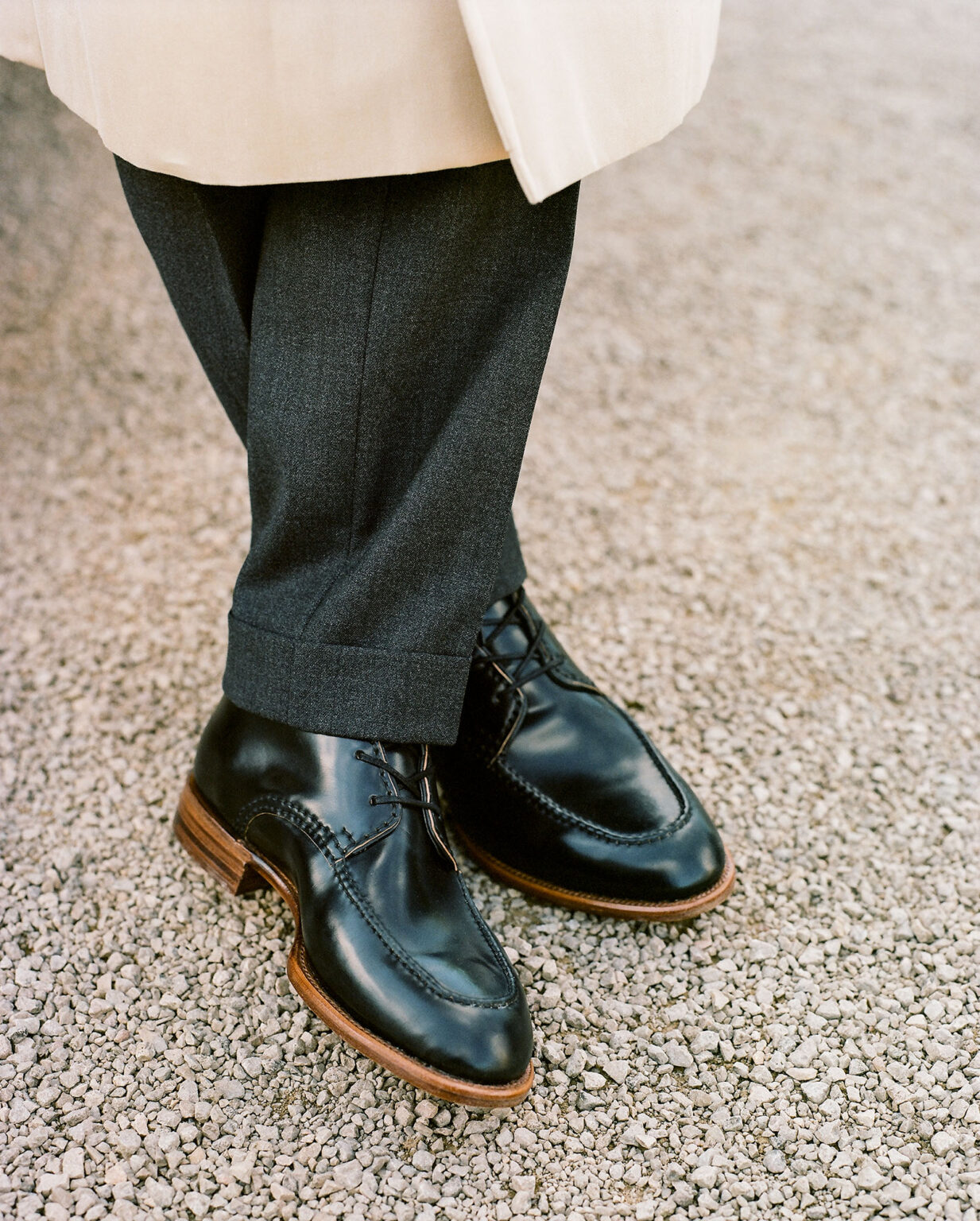 Closeup of gentleman's legs wearing a cream trench coat, grey tailored trousers and a pair of E.Woodford Foxley Padded Ankle Boots in Black Horween Shell Cordovan