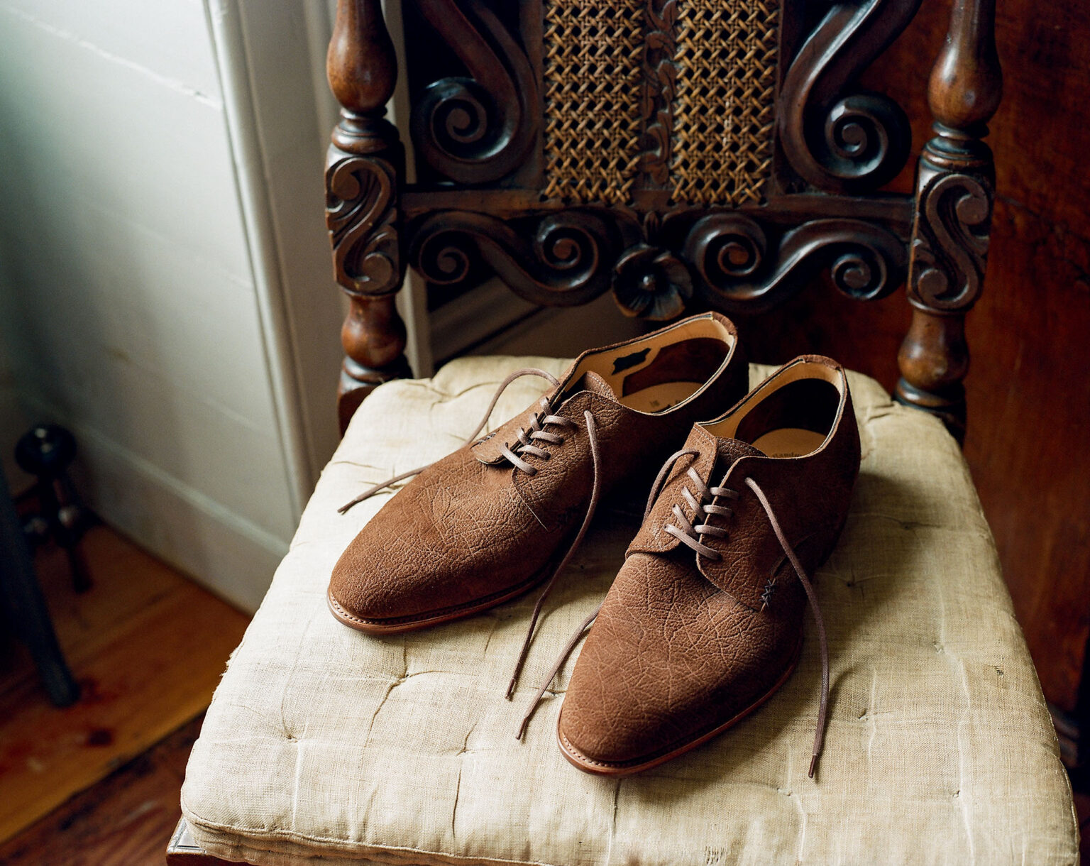 A pair of E.Woodford Kennington Gibsons in Dark Chestnut CF Stead Janus Calf with Ernest emboss sitting on a vintage ornate mahogany chair with an invory cushion