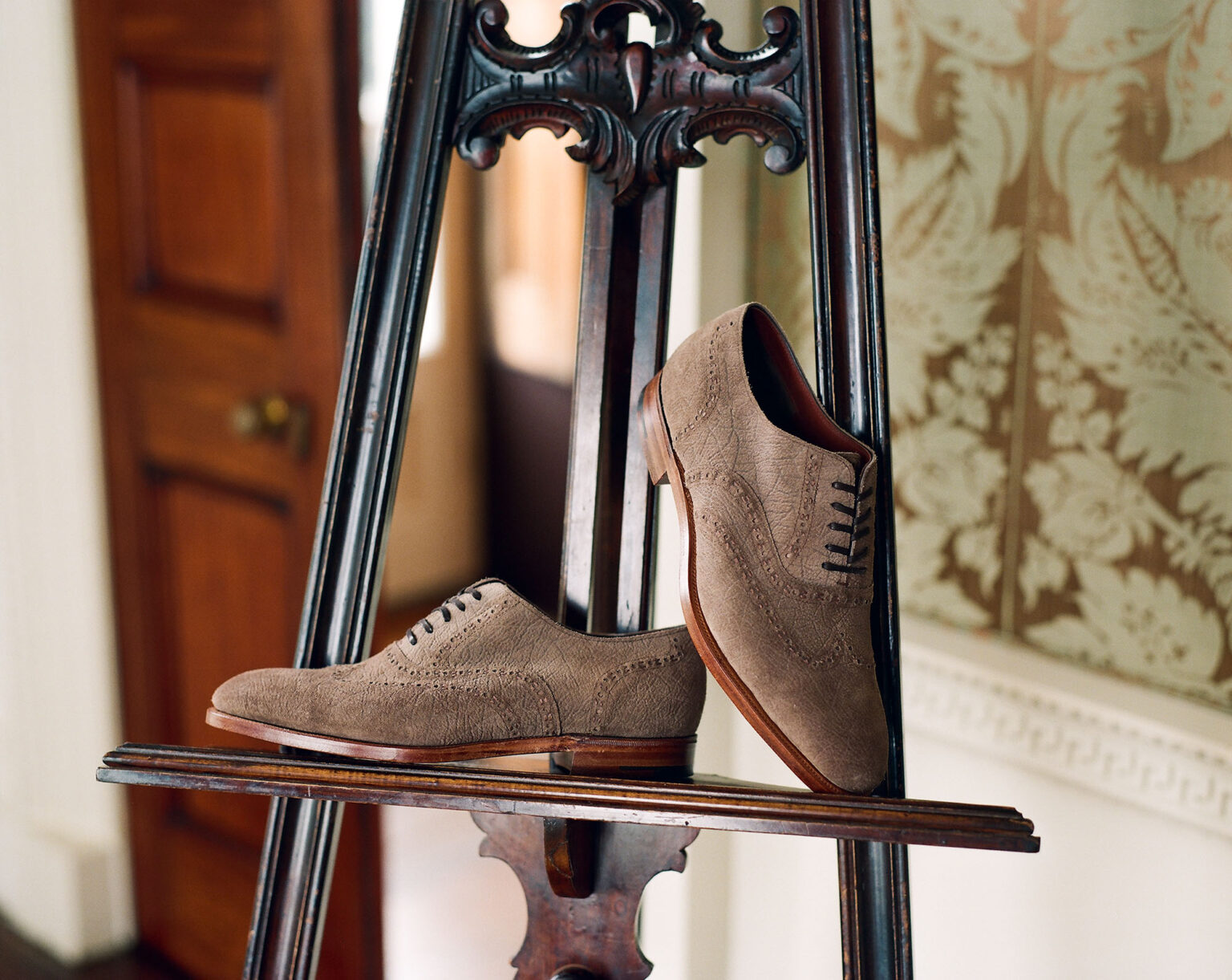 A pair of E.Woodford Redbourne Five Eyelet Oxfords in Fog CF Stead Janus Calf with Ernest emboss resting on a mahogany ornate painter's easel