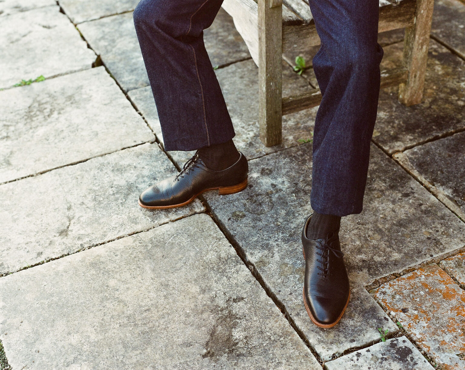 A closeup of a gentleman wearing a pair of E.Woodford Regent Wholecuts in Black Horween Veg Tanned Bison while standing on a wet marbled patio