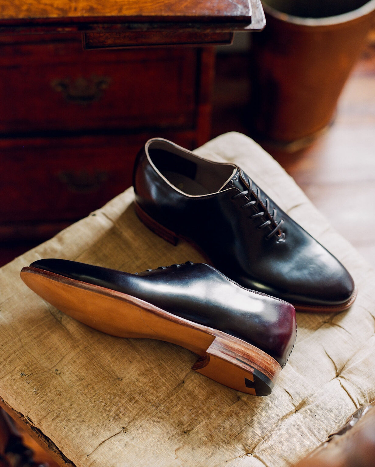 A pair of E.Woodford Regent Wholecuts in No.8 Marbled Horween Shell Cordovan laying on a ivory chair cushion with long evening shadows