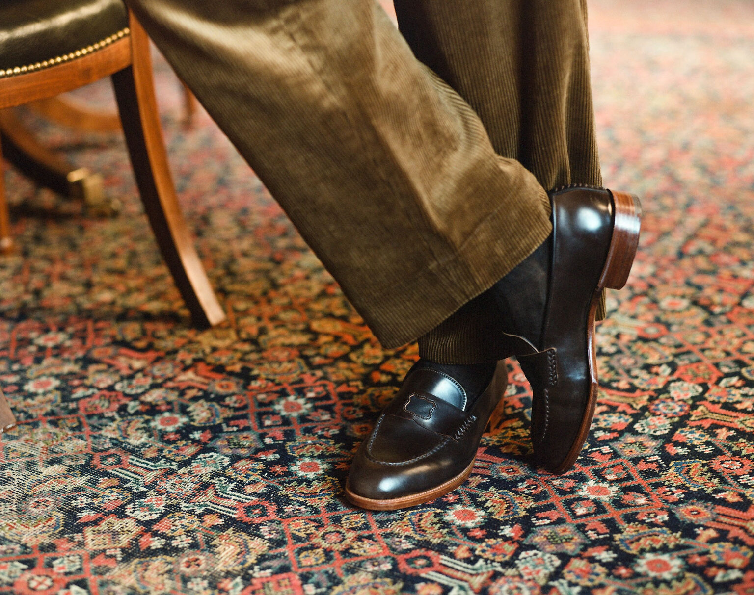 Close up of gentleman standing on an ornate patterned rug weating a pair of E.Woodford Watling Penny Loafers in Dark Cognac Horween Shell Cordovan