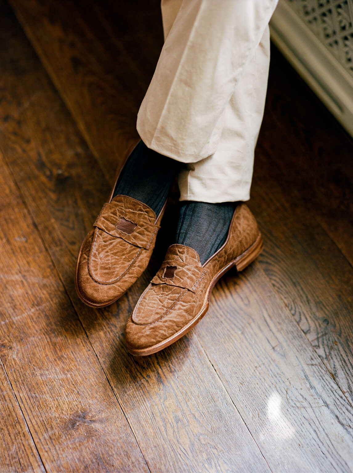 Close up of gentleman wearing E.Woodford Watling Penny Loafers in Dark Chestnut CF Stead Janus Calf standing on a wooden oak floor with sunlight coming through the window and wearing linen trousers