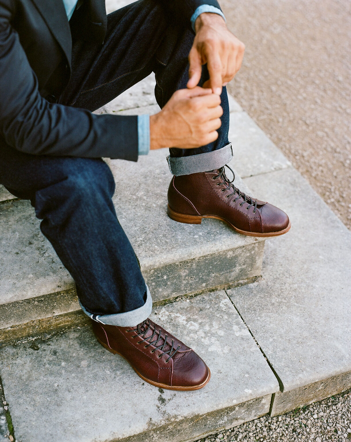 Close of gentleman sitting on patio steps wearing turned up denim jeans and a pair of E.Woodford Woburn Monkey Boots in Nordic Red Horween Veg Tanned Bison