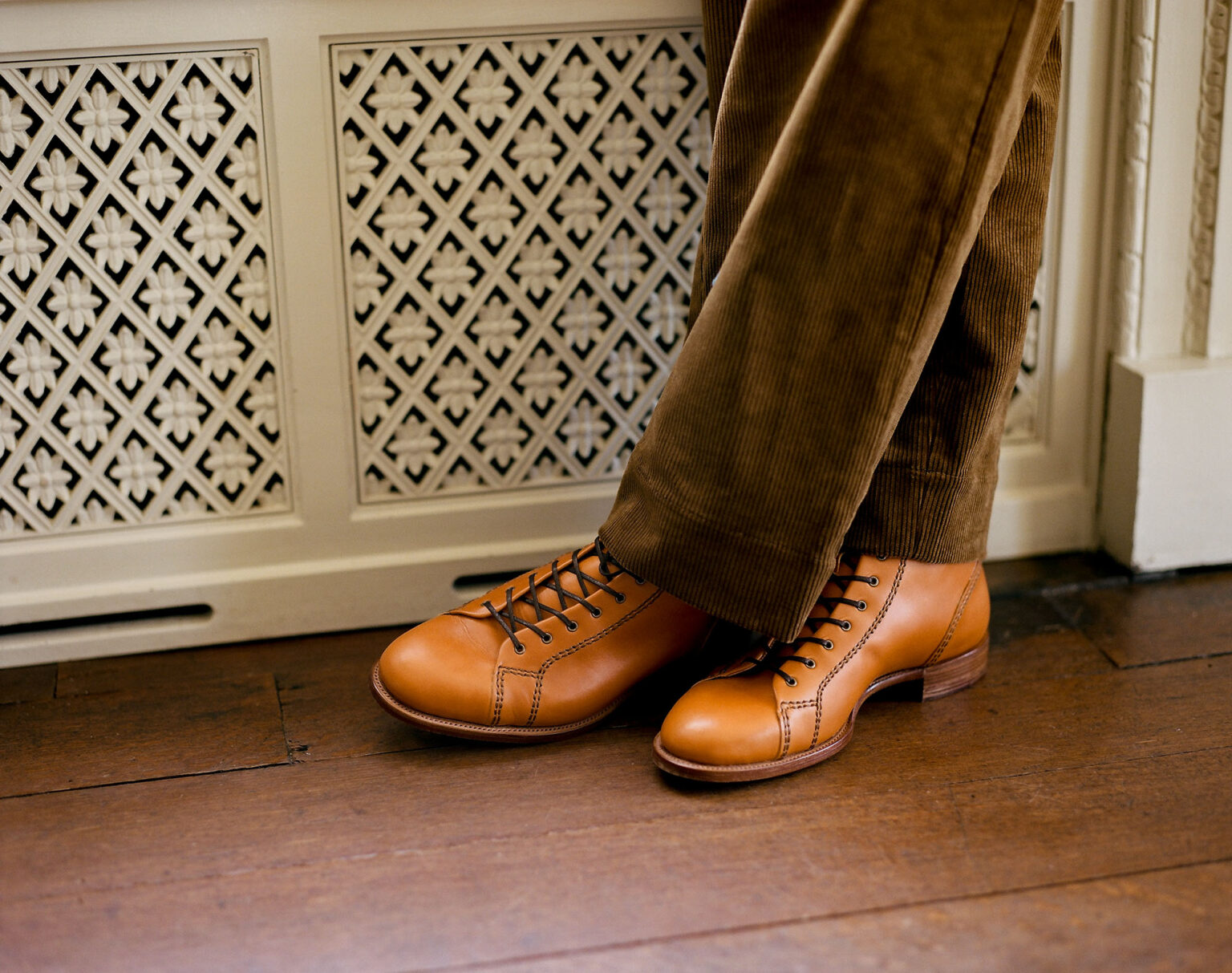 Close up of gentleman wearing brown corduroy trousers and a pair of E.Woodford Woburn Monkey Boots in London Tan J & FJ Baker English Calf standing in front of an ornamental radiator cover